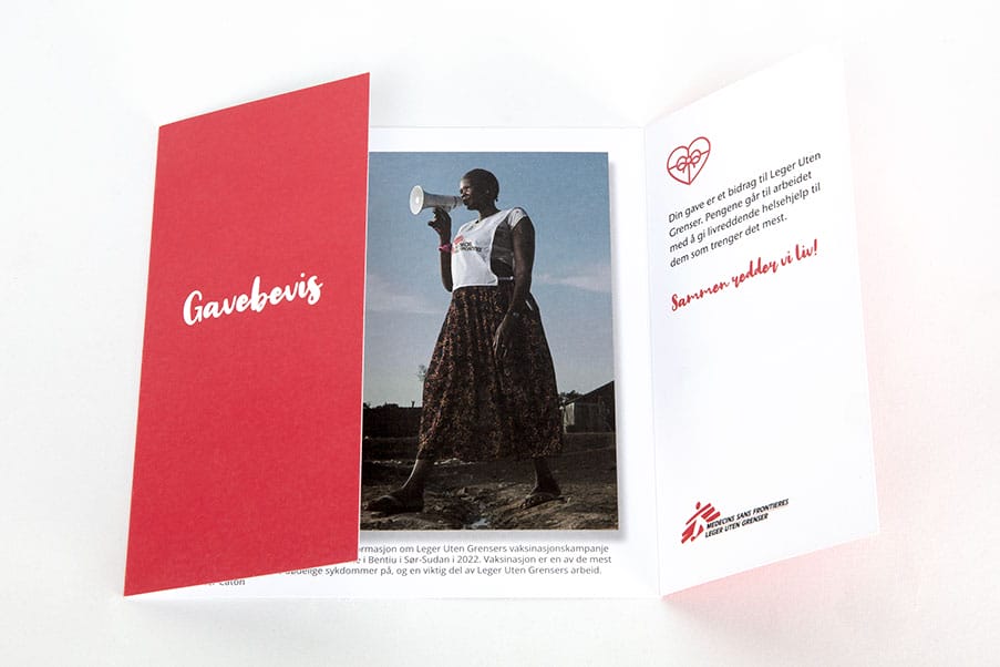 Kort med rød front og teksten "Gavebevis". Høyre flapp er åpen og inni kortet er det bilde av en kvinne ikledd kjole og Leger Uten Grenser-vest.