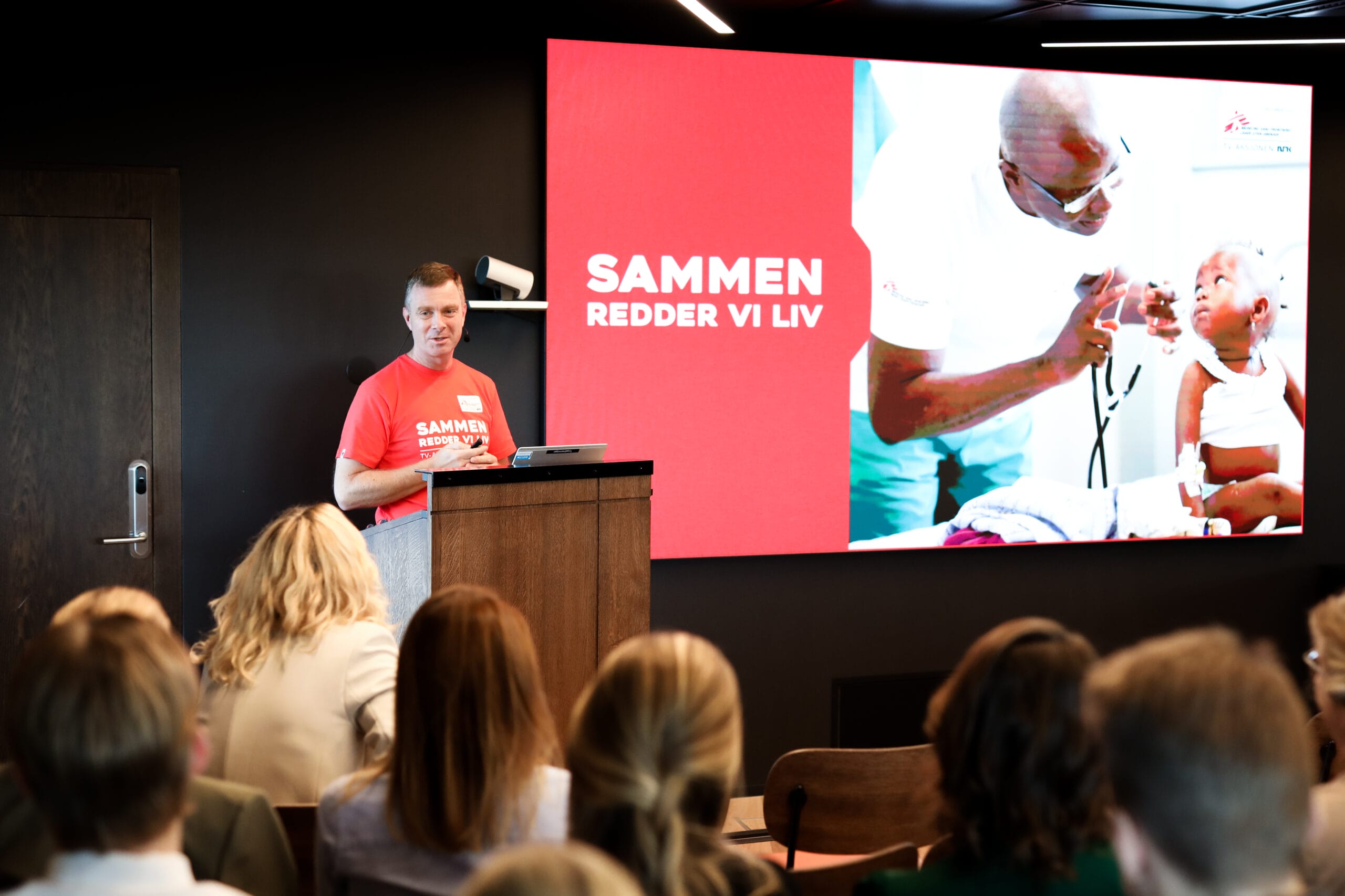 Styremedlem Peter Thyssen holder foredrag. Presentasjonen viser en slide det står "Sammen redder vi liv" på.